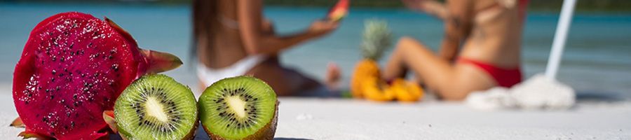 Colourful fruit sitting in white sand with two girls behind in the distance