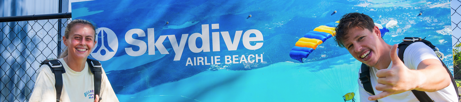 A man and a woman smiling in front of a Skydive sign
