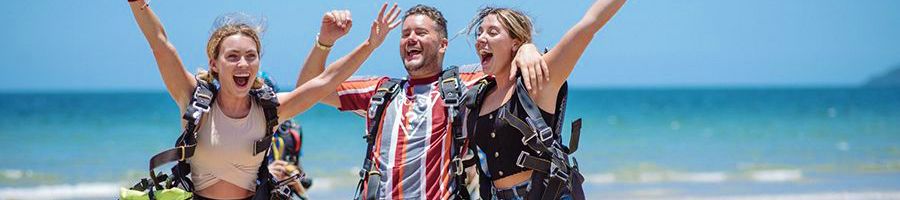 a group of young skydivers post-jump on the beach smiling