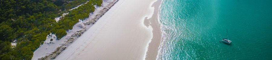 Whitsunday Blue in bright blue waters with white sands and island greenery