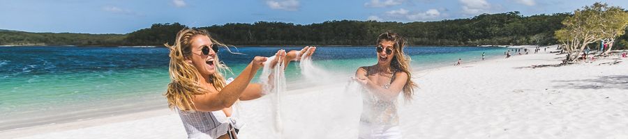 Two girls with sand in their hands standing on a beach