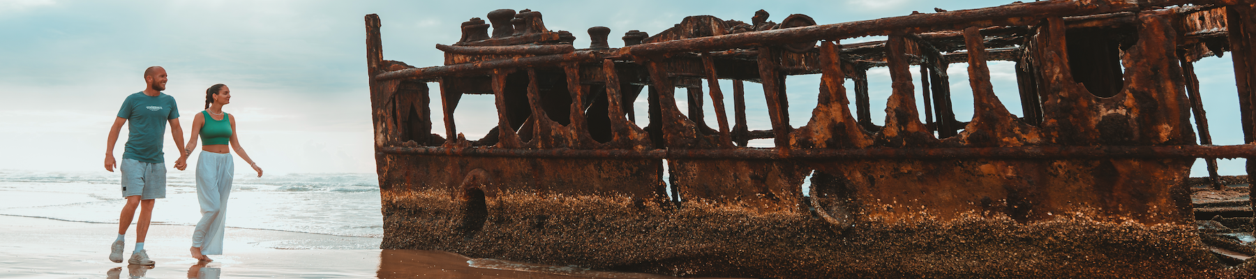 a couple walking hand in hand alongside a shipwreck
