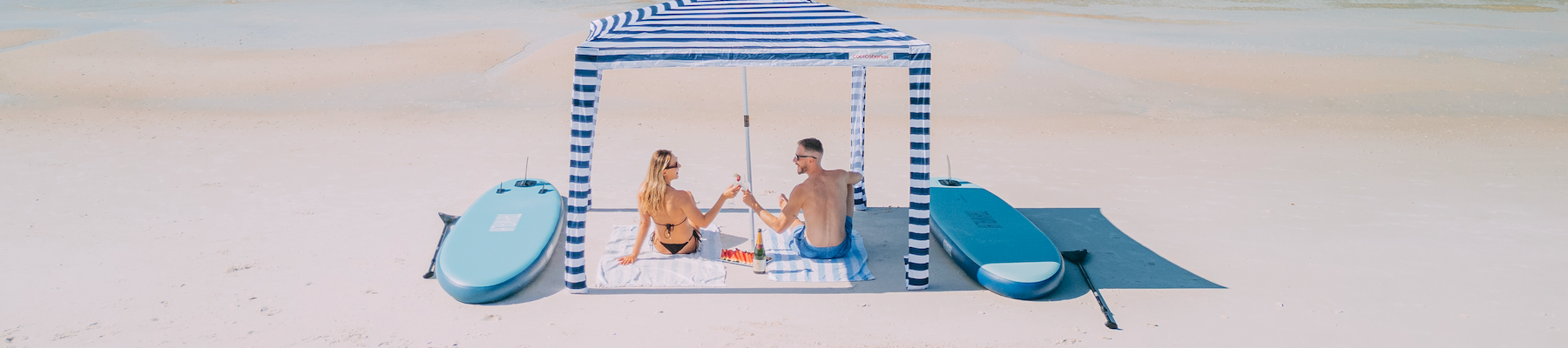 a couple under a cabana on a beach with paddle boards