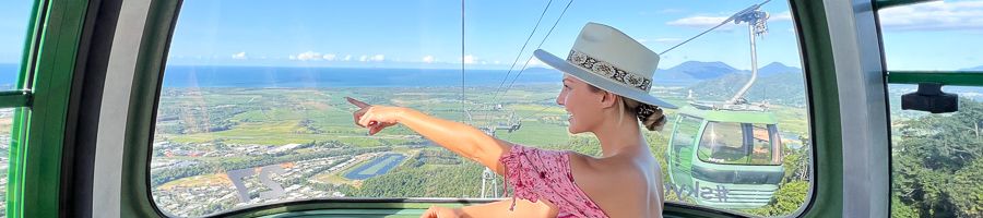 Woman in a pink dress in the skyrail pointing at the view