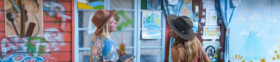 Two women with drinks outside of a colourful building