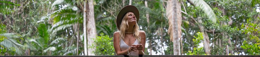 Fraser Island A girl in a hat looking up at trees while standing on a bridge