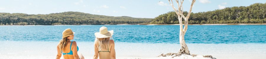 two girls sitting on the white sand at Lake McKenzie