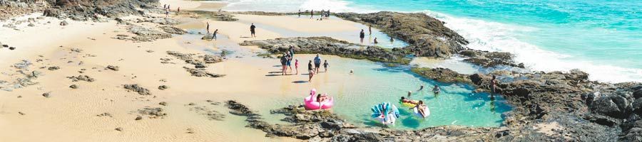 Champagne Pools people swimming in the Champagne Pools near the ocean on K'gari