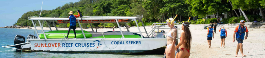 Two women standing on the beach with snorkel gear and glass bottom boat in background.
