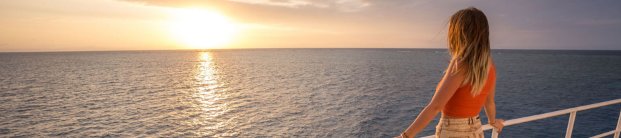 Woman standing on boat deck watching the sunrise/sunset across the water
