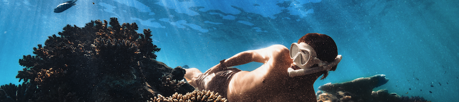 Snorkelling Whitsundays A man with a white snorkel mask on underwater swimming through a reef