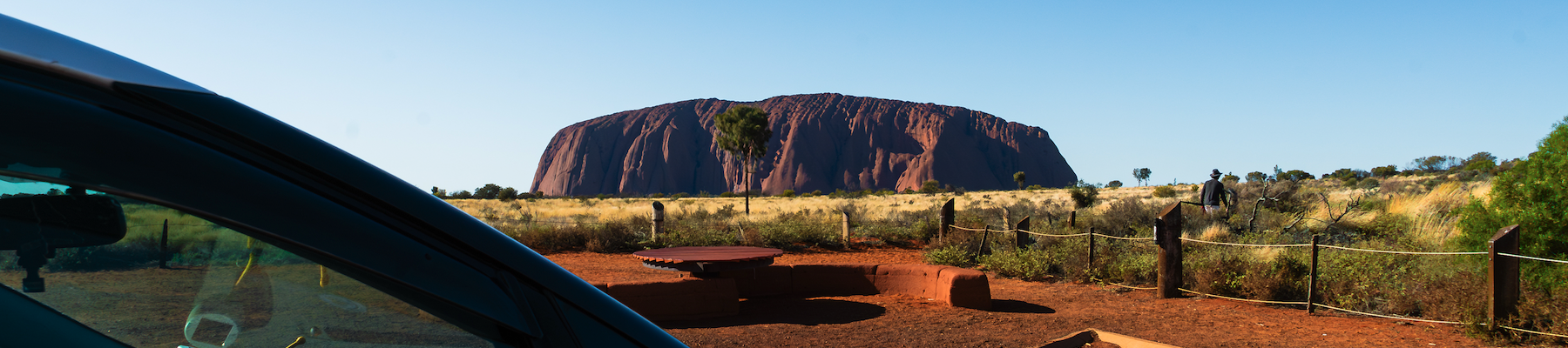 a photo of uluru in the distance taken from the side of a van