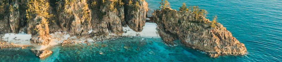 aerial view of rocky cliffs and secluded whitsunday beach
